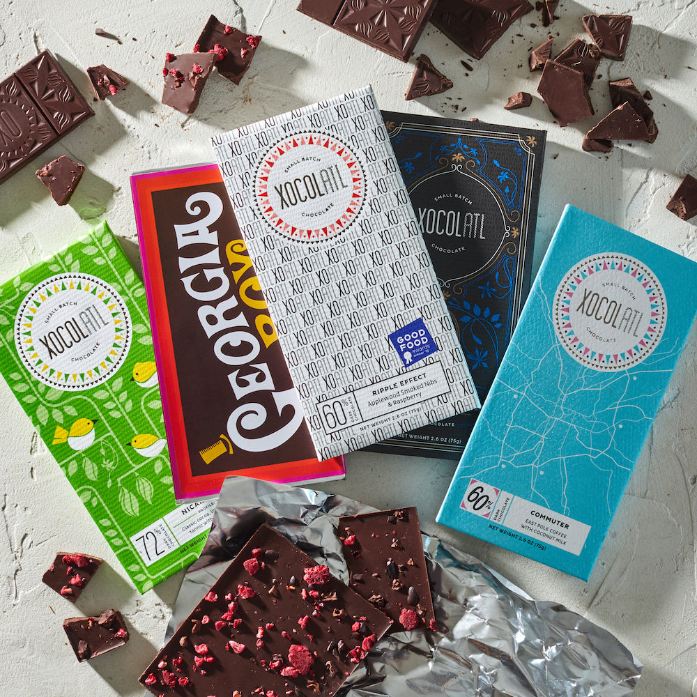 A collection of colorful chocolate bars with various flavors, displayed alongside broken pieces of chocolate. Each bar has unique packaging indicative of its flavor profile.